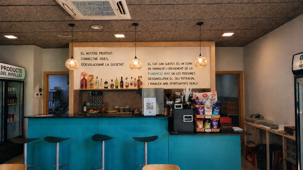 Barra del bar de Can Guetes amb el text "El nostre propòsit: connectar vides, (r)evolucionar la societat" pintat a la paret