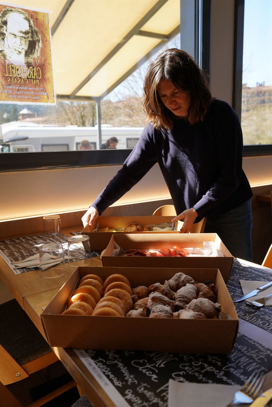 Personal de Can Guetes preparant la taula de la cafeteria amb dolços i producte de proximitat